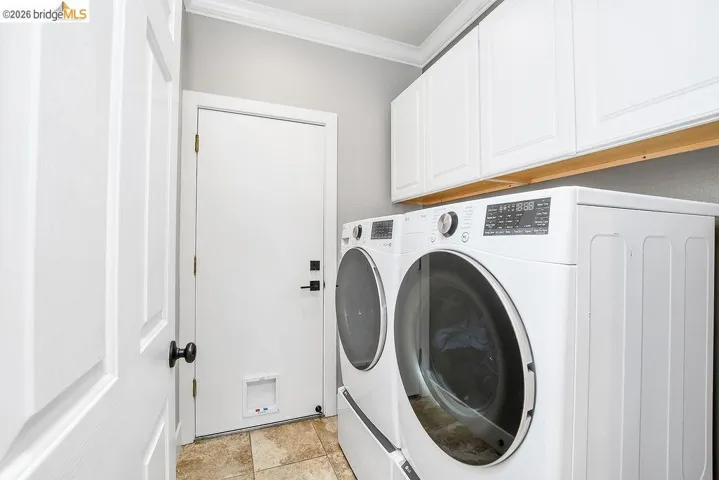Laundry area with overhead white cabinetry, crown molding, and tiled flooring