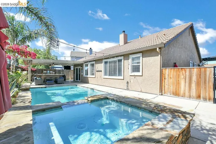Backyard featuring a built-in swimming pool and spa, concrete decking, an outdoor bar area with a pergola, and mature landscaping