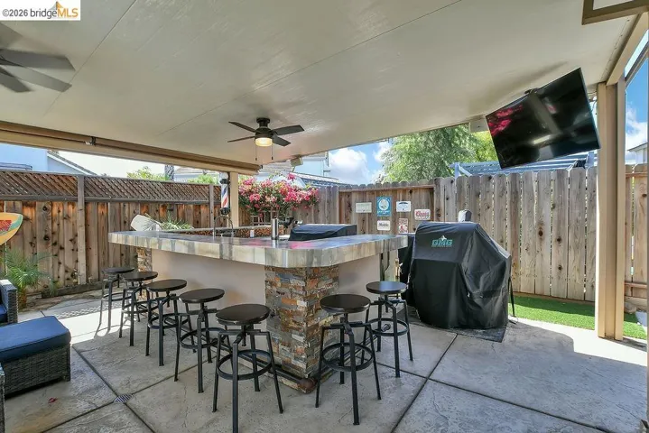 Covered outdoor patio featuring a stone-clad bar, built-in ceiling fans, and a mounted screen