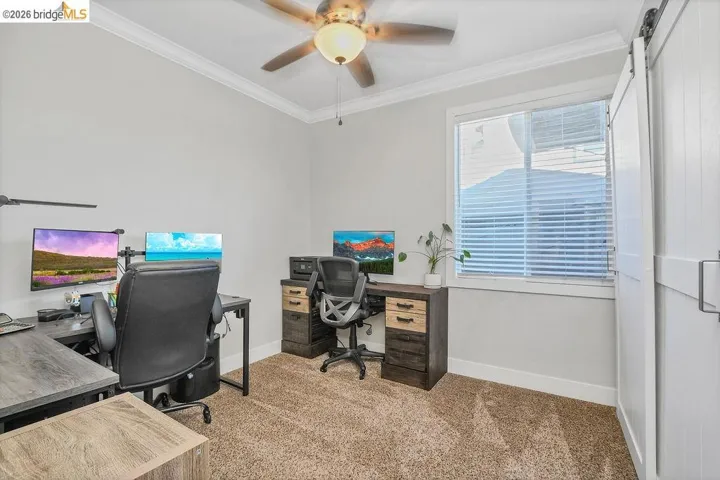 Carpeted room featuring a ceiling fan with light fixture, a window with blinds, crown molding, and a white barn door