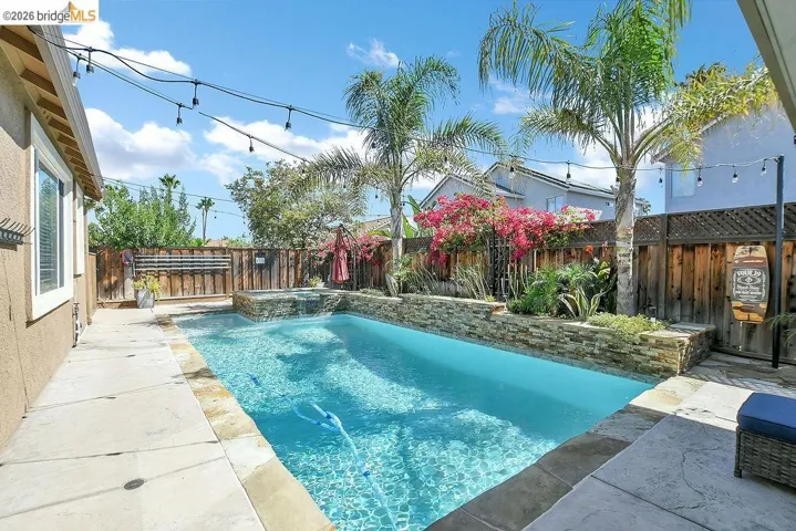In-ground swimming pool with an integrated spa, surrounded by concrete patio decking and natural stone accents