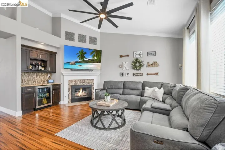 Living area featuring wood-finish flooring, a fireplace with a decorative tile surround and white mantel, and a built-in wet bar with dark wood cabinetry, integrated beverage cooler, and tiled backsplash