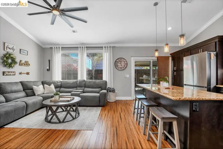 Open-concept living space featuring wood-finish flooring, a contemporary ceiling fan, and multiple windows with blinds