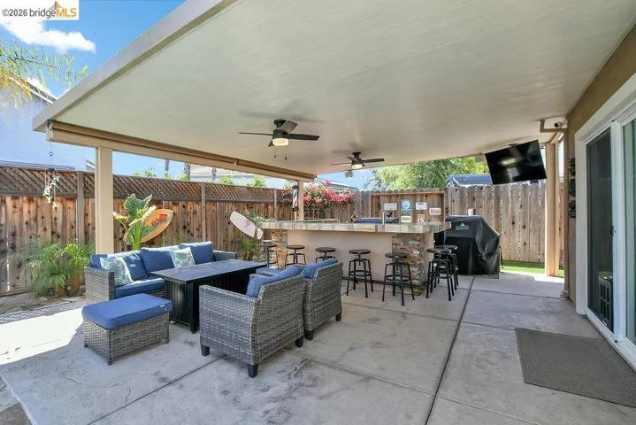 Spacious covered patio featuring a built-in bar with stone veneer accents, integrated ceiling fans, and a mounted outdoor television