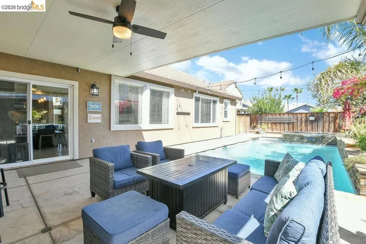 Covered patio with an outdoor ceiling fan, concrete flooring, and sliding glass doors leading indoors