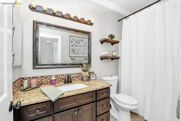 Bathroom featuring a dark wood-finish vanity with a granite-style countertop, mosaic tile backsplash, and an integrated rectangular sink