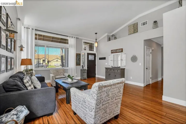 Spacious living area featuring wood-finish flooring, vaulted ceilings, and a large front window with upper transom details
