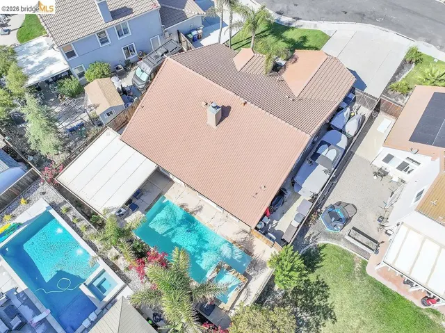 Aerial perspective highlighting a large swimming pool with an integrated spa, expansive paver patio, a detached covered patio structure, and mature landscaping