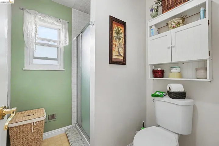 Bathroom featuring a wall-mounted white storage cabinet with open shelving, a toilet, and a window providing natural light