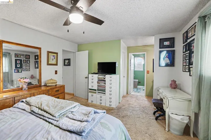 Carpeted room featuring a ceiling fan with integrated lighting, a light green accent wall, and a doorway leading to a bathroom with patterned flooring