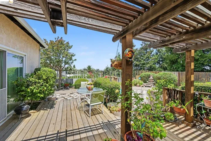 Expansive outdoor deck featuring a wooden pergola, sliding glass door access to the interior, and mature landscaping