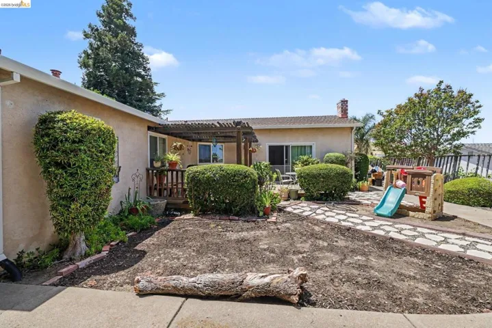Expansive backyard featuring a stone pathway, a deck with a wood pergola, mature hedging, and a stucco exterior