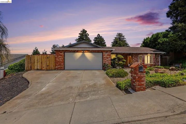 Brick facade residence featuring an attached garage, a paved driveway, and mature landscaping