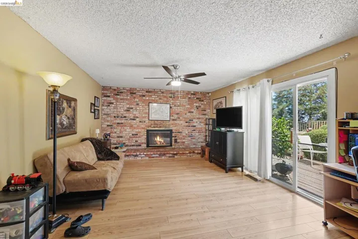 Spacious living area featuring wood-finish flooring, a brick-faced fireplace, and a ceiling fan