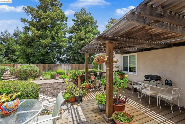 Backyard featuring a wooden pergola-covered deck, manicured hedges, a wooden privacy fence, and mature trees