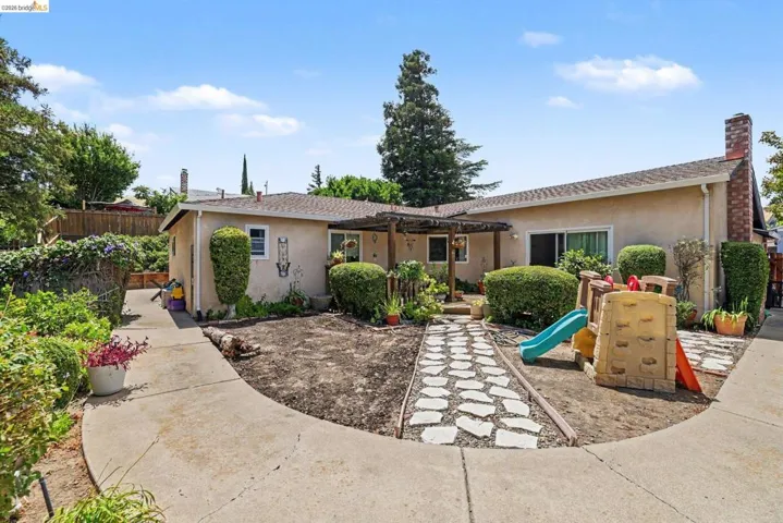 Stucco exterior featuring a covered entry, concrete pathways, stone step path, and mature landscaping