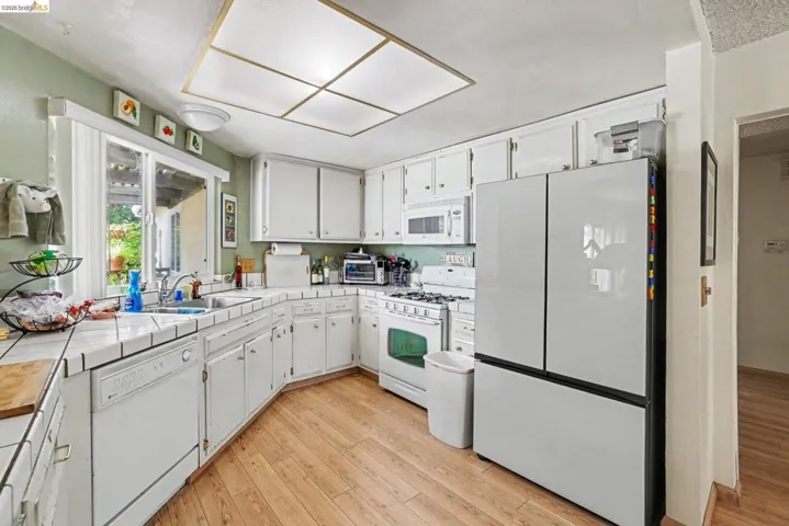 Kitchen featuring wood-finish flooring, white cabinetry, tile countertops, and a full suite of white appliances