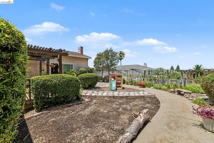 Expansive backyard featuring a concrete pathway, mature perimeter landscaping, and a flagstone patio area