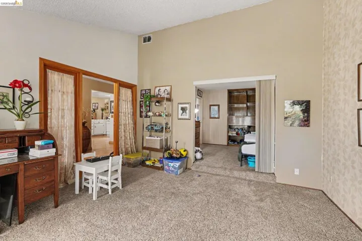 Spacious room featuring vaulted ceilings, textured carpeting, and dual doorway openings with wood trim