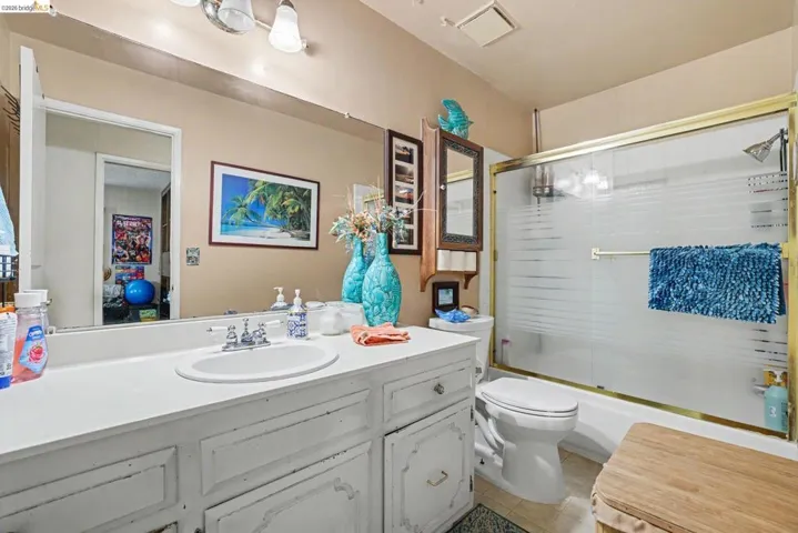 Bathroom featuring a vanity with an integrated sink, a framed mirror, a tub-shower combination with sliding frosted glass doors, and a toilet