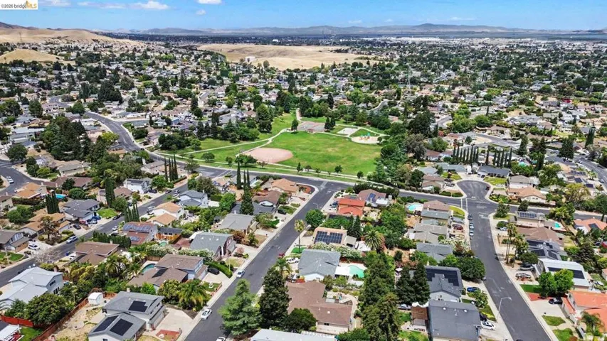 Expansive residential community featuring mature trees, a central green space with a baseball diamond, and paved streets