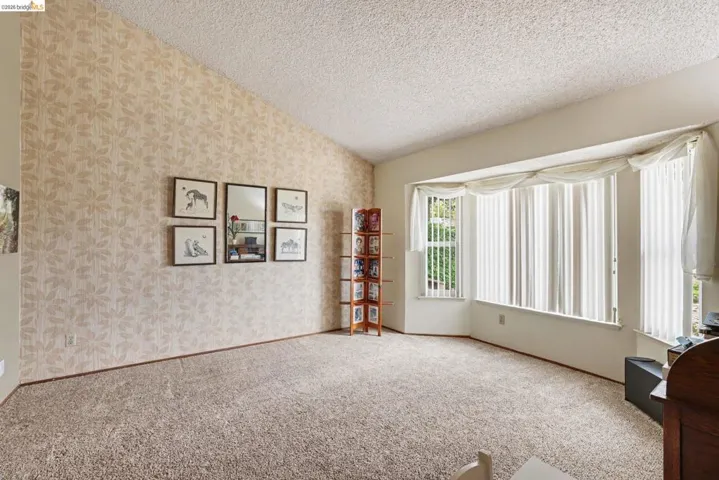 Bay window with vertical blinds, angled ceiling, patterned accent wall, and textured carpeting