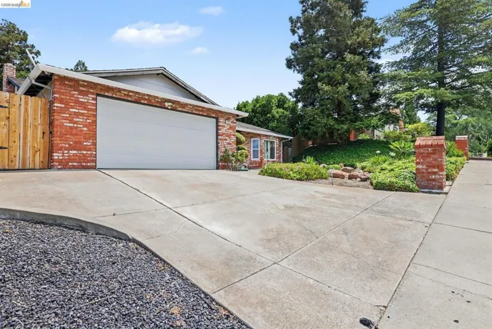 Brick facade home featuring a two-car garage, concrete driveway, and mature landscaping