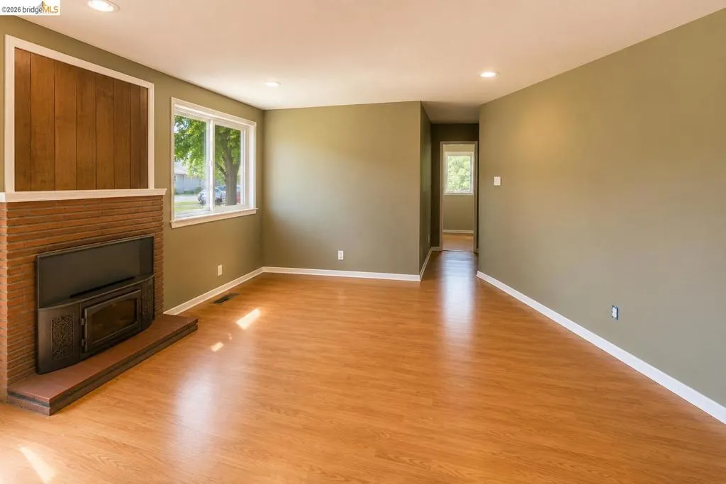 Spacious living area featuring wood-finish flooring, recessed lighting, and a brick-faced fireplace with a wood-paneled accent wall