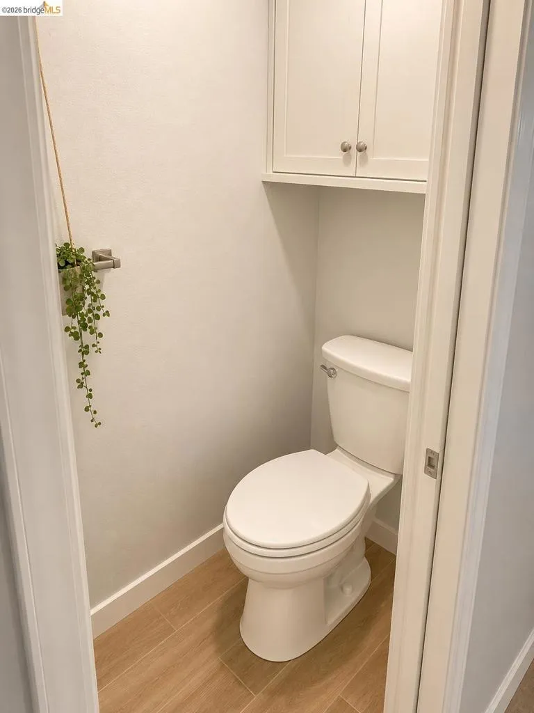 Dedicated water closet featuring a white toilet, wood-finish tile flooring, and integrated white cabinetry with nickel hardware