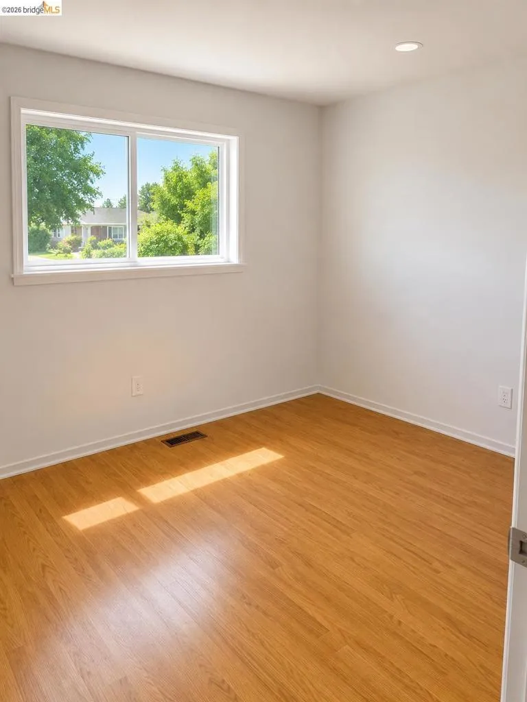 Bright room featuring wood-finish flooring, a white window frame, and recessed ceiling lighting