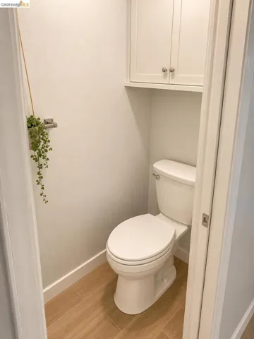 Dedicated water closet featuring a white toilet, wood-finish tile flooring, and integrated white cabinetry with nickel hardware
