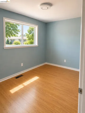 Room with light blue walls, wood-finish flooring, a white trim window, and a modern flush-mount ceiling light fixture