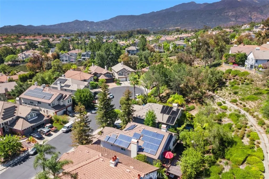 This impressive aerial view showcases the home's solar panels, tile roof, and private setting nestled among lush mature trees with the stunning Saddleback Mountains as a backdrop. Surrounding trails and the beautifully maintained guard gated community are visible in every direction.