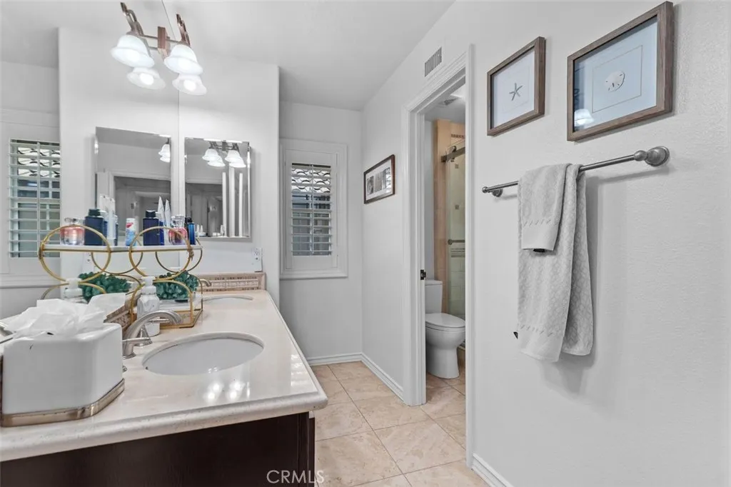 The Jack and Jill bathroom also features travertine tile flooring, and a private water closet with step in travertine shower enclosed in glass. Plantation shutters and a clean bright finish complete this thoughtfully designed and generously sized shared bath.