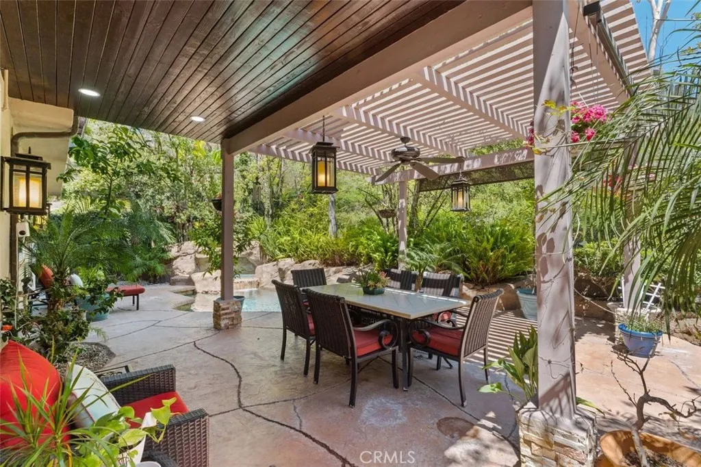 The covered poolside lanai features a pergola with ceiling fan, pendant lantern lighting, and a generous dining and lounge area ideal for year round outdoor entertaining with French doors connecting seamlessly to the interior.
