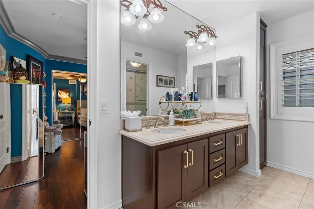 The Jack and Jill bathroom serving the upper level bedrooms features a dual sink travertine vanity, dark cabinetry with gold hardware, large mirror, a dedicated linen closet, and plantation shutters for natural light.
