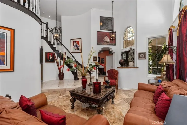 The dramatic two story great room impresses with soaring vaulted ceilings, elegant travertine tile floors, crown molding, and a sweeping staircase with dark wood railings. Arched doorways and a second floor loft overlooking the space below add architectural grandeur throughout.