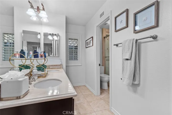 The Jack and Jill bathroom also features travertine tile flooring, and a private water closet with step in travertine shower enclosed in glass. Plantation shutters and a clean bright finish complete this thoughtfully designed and generously sized shared bath.