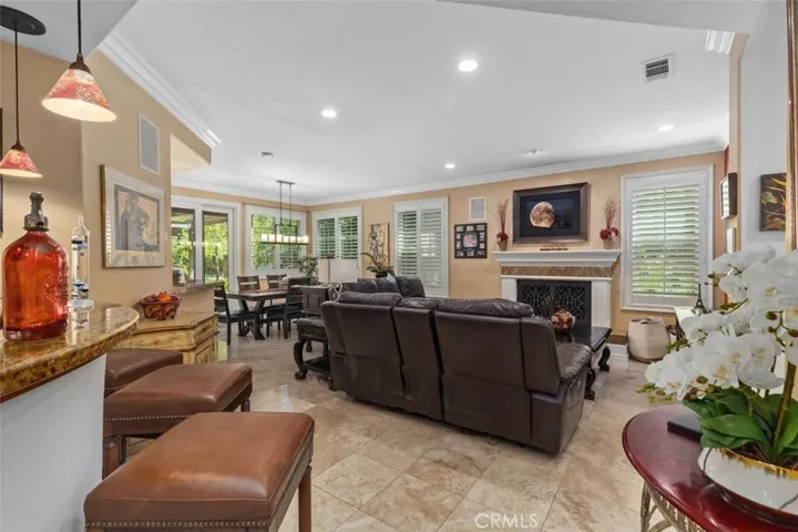 The spacious family room with fireplace flows openly to the casual dining area and granite topped bar with pendant lighting, creating an ideal layout for everyday living and entertaining. Crown molding, travertine tile floors, plantation shutters, and recessed lighting throughout add a polished finish to this central living space.