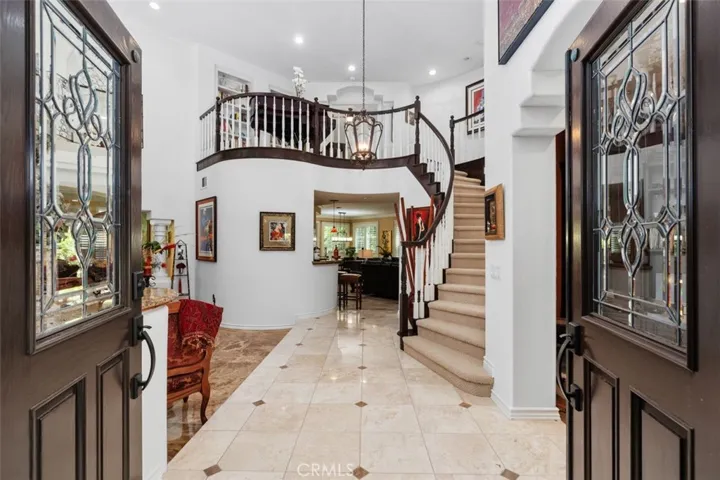 Step through the dramatic double doors with leaded glass panels into a soaring two story foyer that immediately impresses with travertine tile floors featuring inlaid detail, a graceful curved staircase, and an elegant pendant chandelier. The upper level loft and curved balcony overlooking the entry below set the tone for the refined character found throughout every room of this exceptional home.