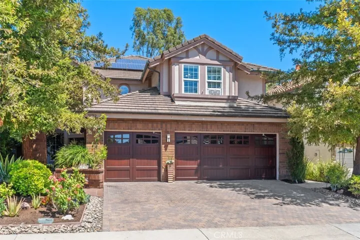 The impressive curb appeal features a custom brick paver driveway and approach, craftsman style wood garage doors, and professionally landscaped grounds framed by mature trees.