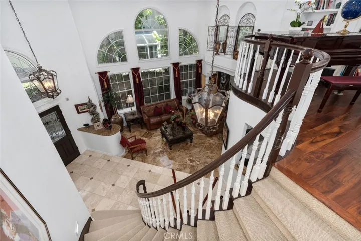 The sweeping staircase makes a stunning architectural statement as it curves gracefully from the upper loft down to the travertine tiled great room below. Soaring two story windows, an elegant pendant chandelier, and arched transom details above the double door entry are all visible from this breathtaking vantage point.