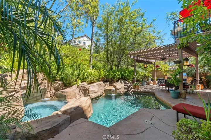 The resort style backyard retreat features a custom pool with cascading rock waterfall, spa, and lush mature professional landscaping. A covered poolside lanai with ceiling fan and pendant lanterns provides the perfect setting for outdoor dining and entertaining.