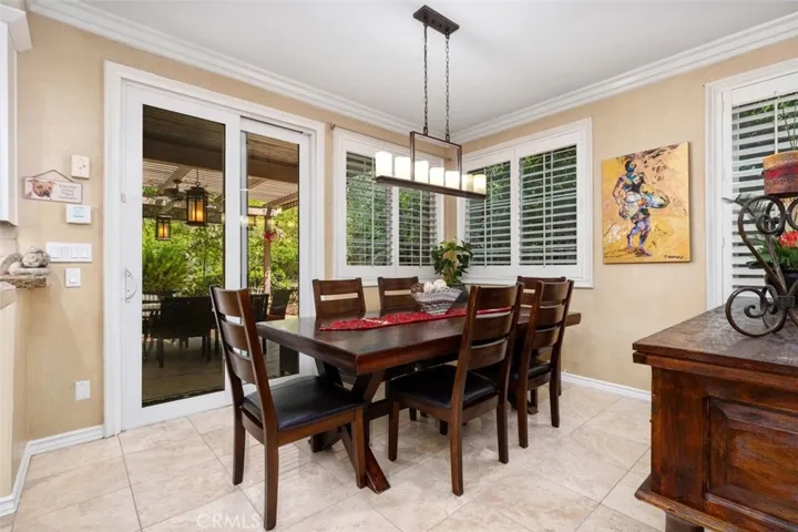 The bright and airy casual dining area features crown molding, travertine tile floors, plantation shutters, and a stylish linear pendant chandelier. French doors open directly to the covered poolside lanai, creating an indoor outdoor flow perfect for everyday dining and entertaining.