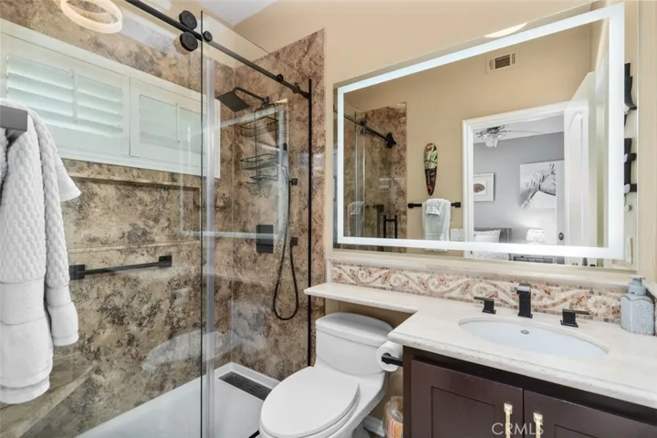 This beautifully updated ensuite bath features a step in shower with richly veined stone tile, a sleek sliding glass enclosure, and matte black fixtures. A lighted vanity mirror and mosaic tile backsplash detail elevate the space to boutique hotel quality.