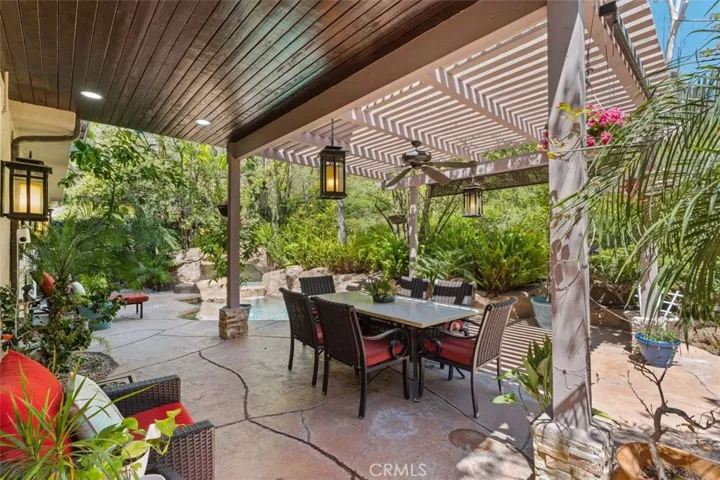 The covered poolside lanai features a pergola with ceiling fan, pendant lantern lighting, and a generous dining and lounge area ideal for year round outdoor entertaining with French doors connecting seamlessly to the interior.