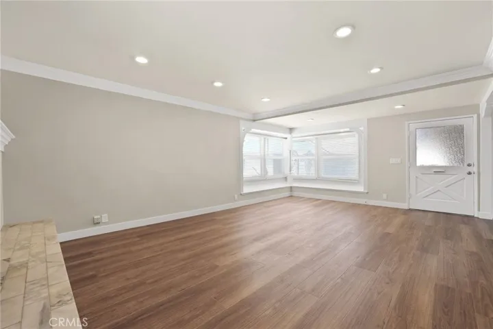 View of living room from opposite side showing the corner window seat and original oversized front door with window panel.