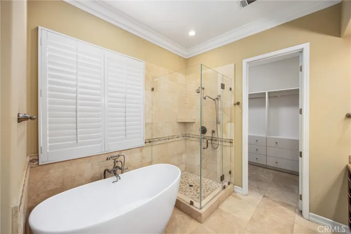 Spa-inspired primary bathroom with freestanding soaking tub, frameless glass shower, and walk-in closet access