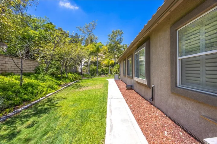Private backyard featuring a manicured lawn, mature landscaping, and a concrete walkway that provides convenient access around the home