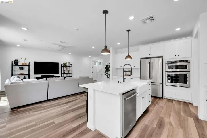 Open-concept kitchen featuring an island with a farmhouse sink, stainless steel appliances, white cabinetry, and wood-finish flooring throughout